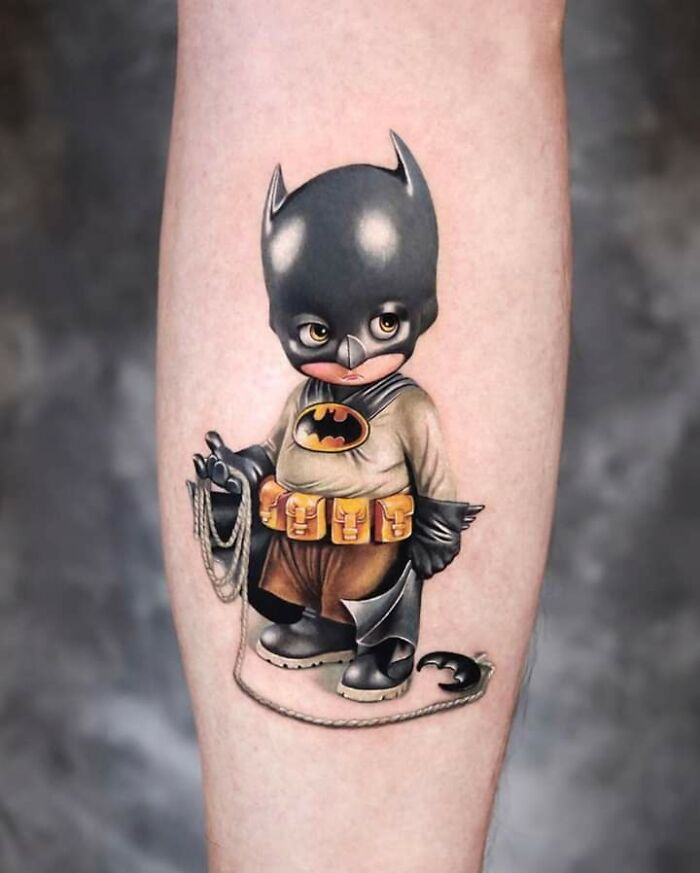 Creative tattoo design of a cartoonish Batman character on someone's calf.