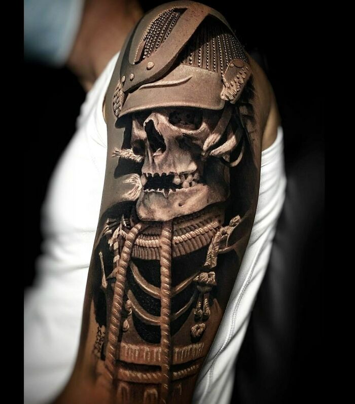 Samurai-themed tattoo design on arm, featuring an intricate skull helmet and armor details.