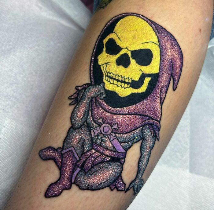 Glitter tattoo of a cartoon-style skeleton in purple and yellow tones on a person's arm.
