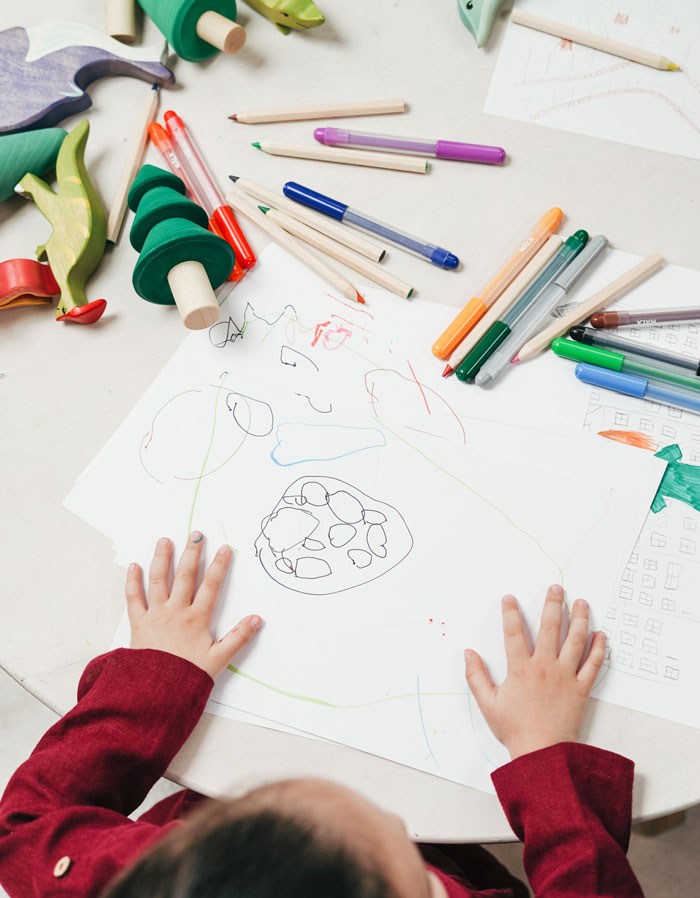 Child drawing abstract shapes with markers and colored pencils on paper surrounded by art supplies for curious art facts.