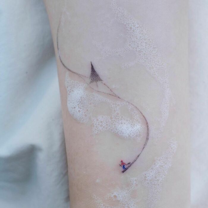 Minimal tattoo design of a delicate kite flying across the skin with bubbles.