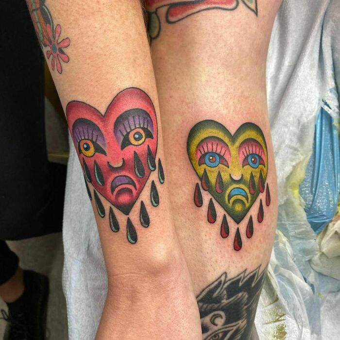 Colorful best friend tattoos with heart faces and teardrops on two arms.
