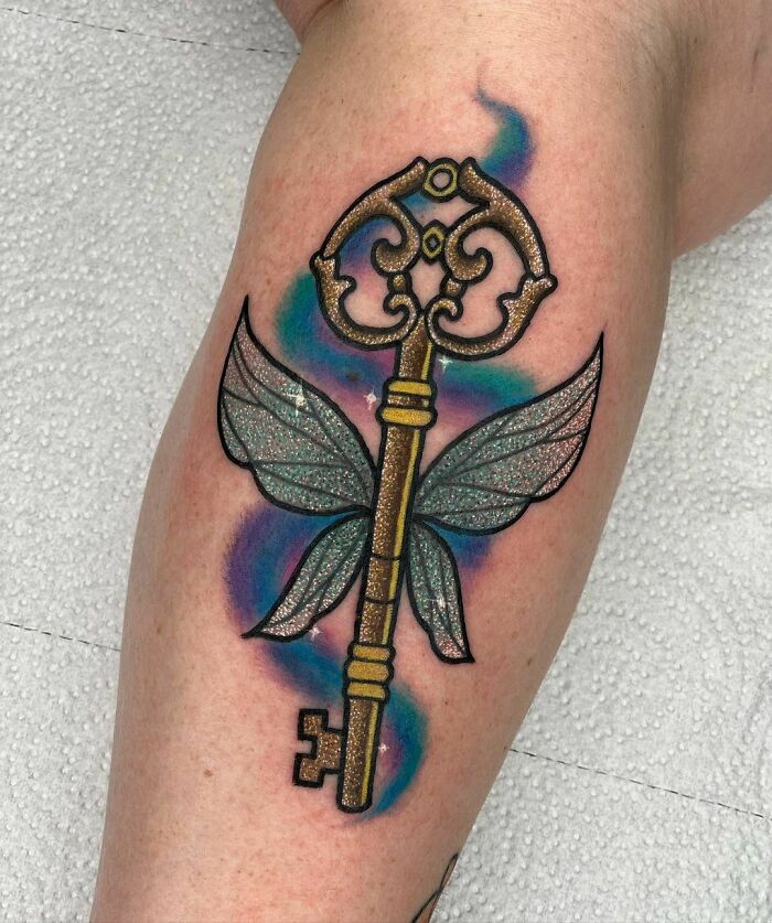 Glitter tattoo of a golden key with wings, highlighting unique and cool design elements.