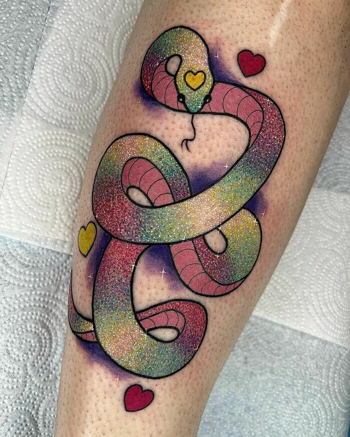 Colorful glitter tattoo of a snake with heart accents on a leg.