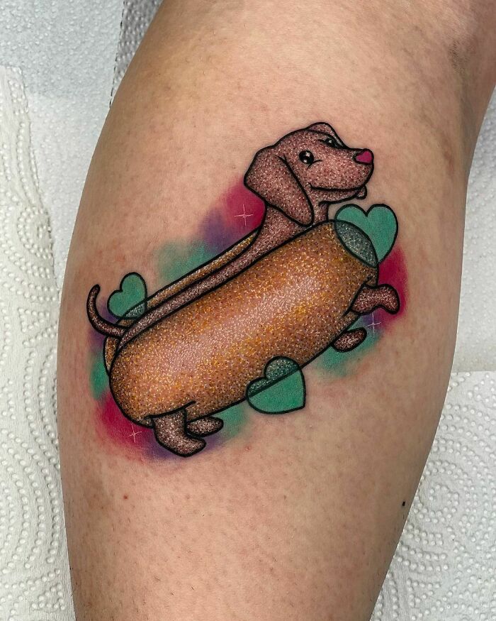 Cute glitter tattoo of a dachshund with hearts on a person's skin.