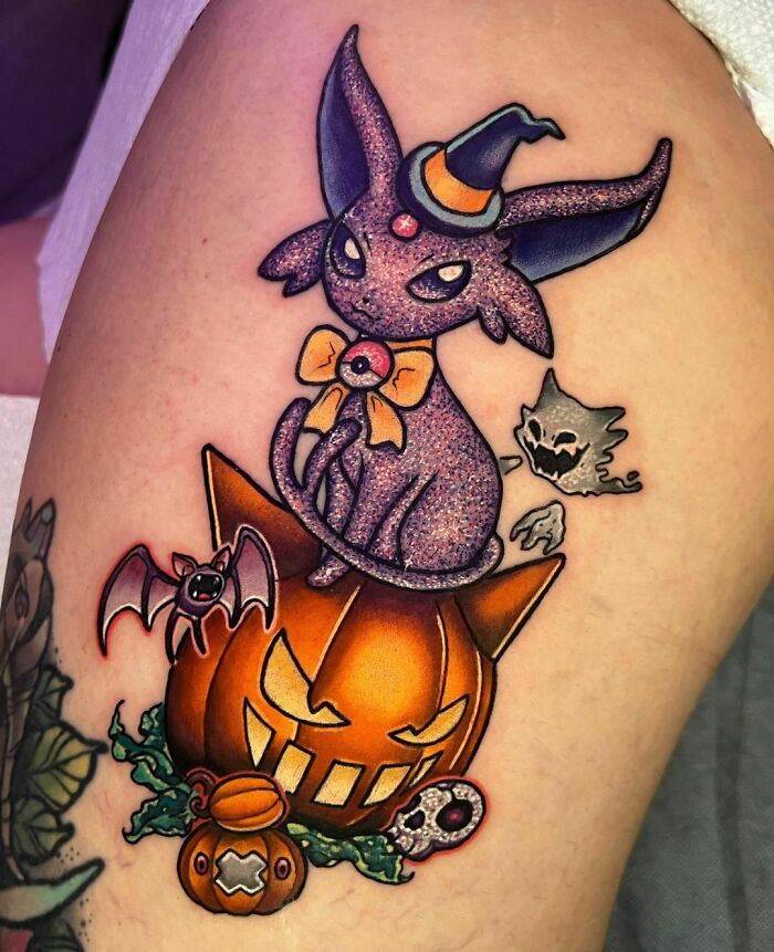 Glitter tattoo of a magical cat with a witch hat on a pumpkin, featuring Halloween-themed elements.