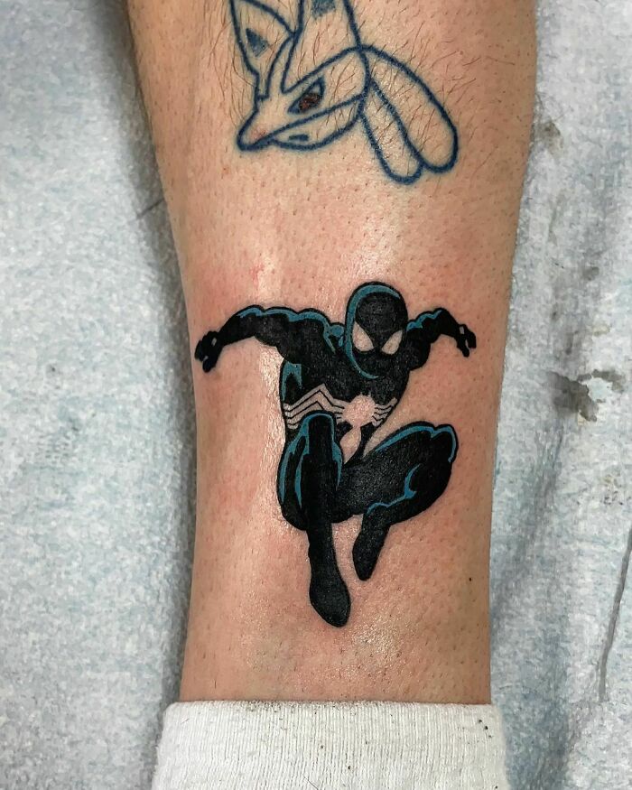 Marvel tattoo featuring Spider-Man in black suit, crouching, above another small character tattoo.