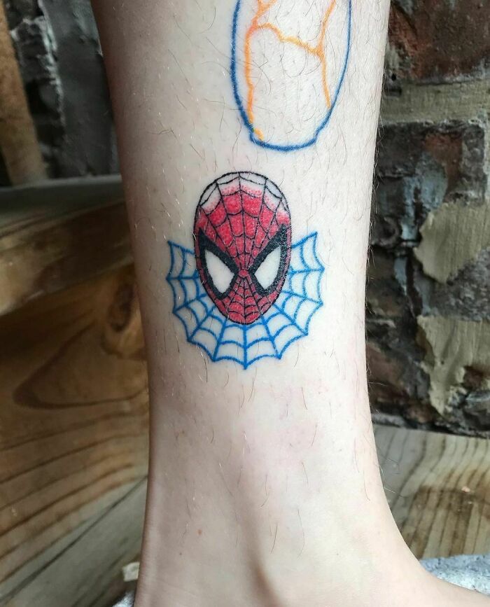 Spiderman tattoo on leg with web design, showcasing vibrant Marvel art.