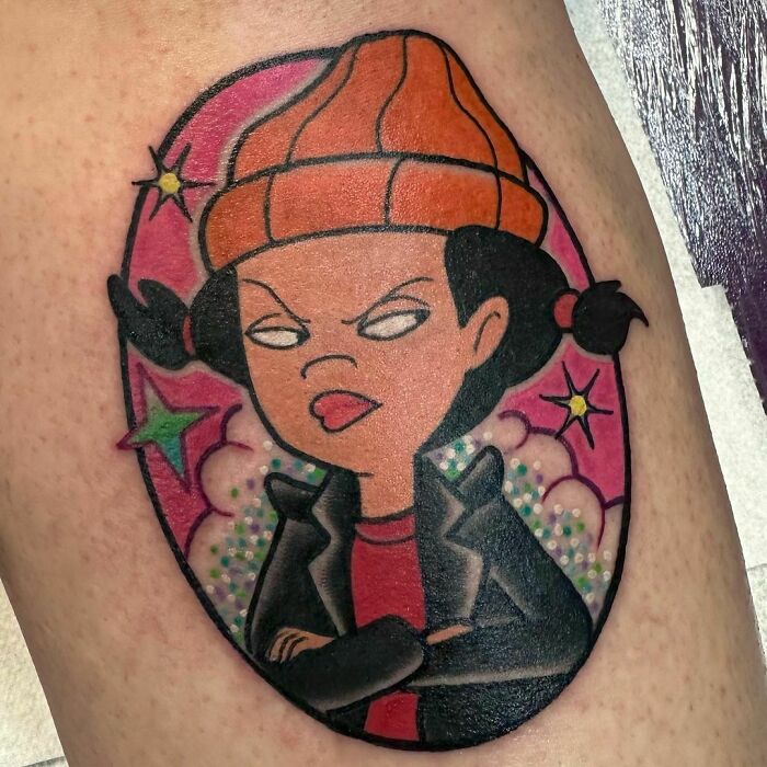 Cartoon tattoo of a character in an orange beanie and leather jacket, inspired by animated shows.