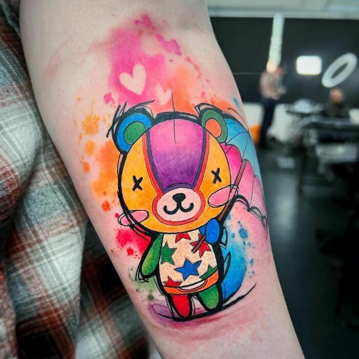 Colorful cartoon tattoo of a cute bear with stars and hearts, inspired by animated shows, on a person's arm.