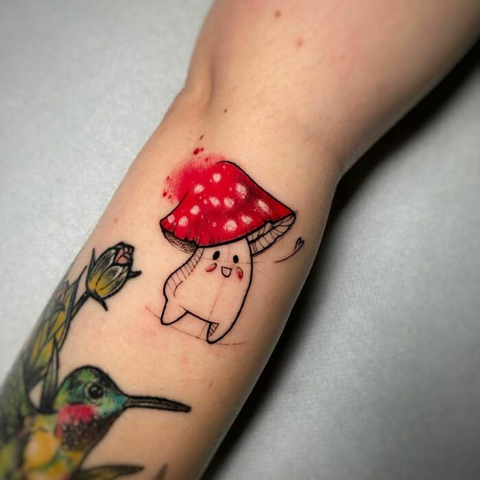 Cartoon tattoo of a smiling tooth with a mushroom cap and arms, symbolizing childhood favorites on an arm.