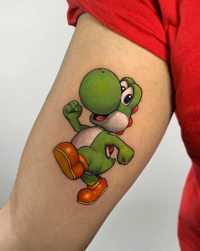 Cartoon tattoo of a green dinosaur character Yoshi on a person's arm, showcasing vibrant colors and playful nostalgia.