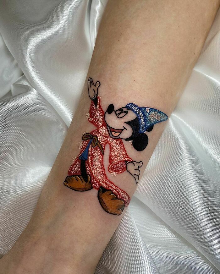 Cool glitter tattoo of a cartoon character in a wizard hat and robe on an arm.