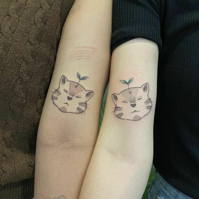 Matching best friend tattoos of cat faces with sprout motifs on forearms.
