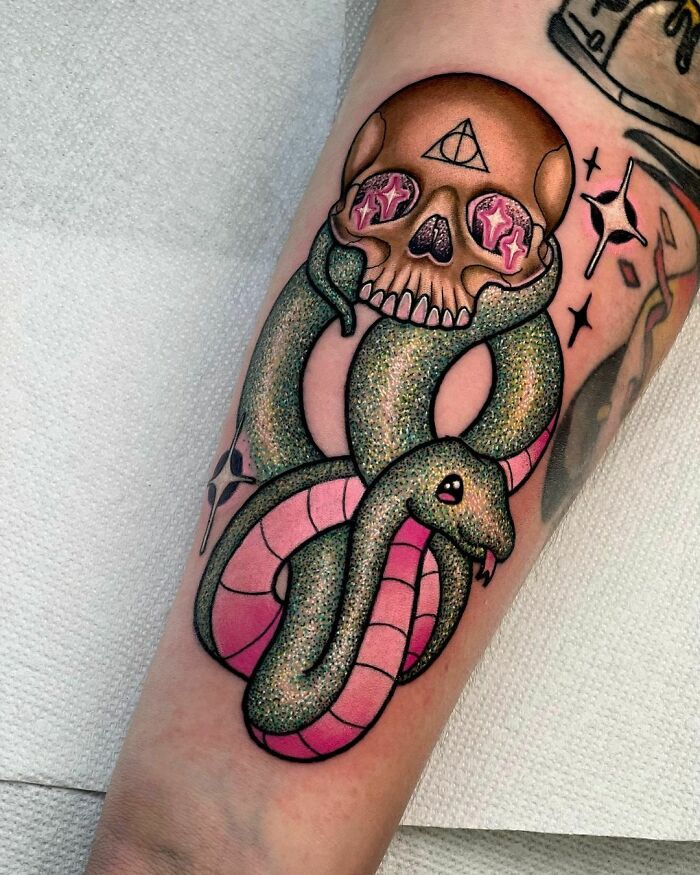 Glitter tattoo featuring a skull with starry eyes and a shimmering snake wrapped around it on an arm.