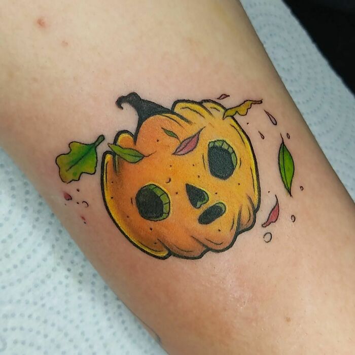 Cartoon-inspired tattoo of a whimsical pumpkin with leaves on an arm.