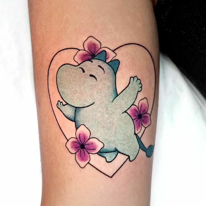 Cartoon tattoo of a joyful character Moomins with flowers, enclosed in a heart shape.
