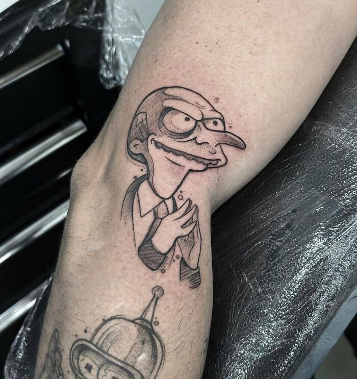 Cartoon tattoo of a suited character on an arm, reminiscent of childhood favorites.