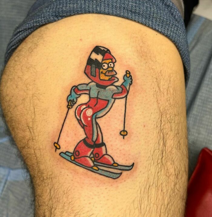 Cartoon tattoo of animated skier character in vibrant colors on a person's thigh.