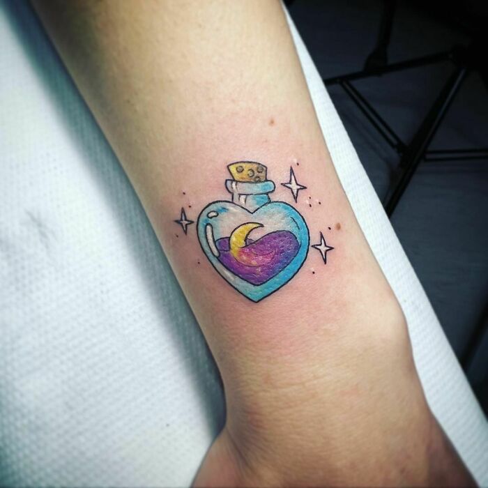 Heart-shaped cartoon tattoo with stars and a crescent moon, inspired by childhood favorites, on a person's forearm.