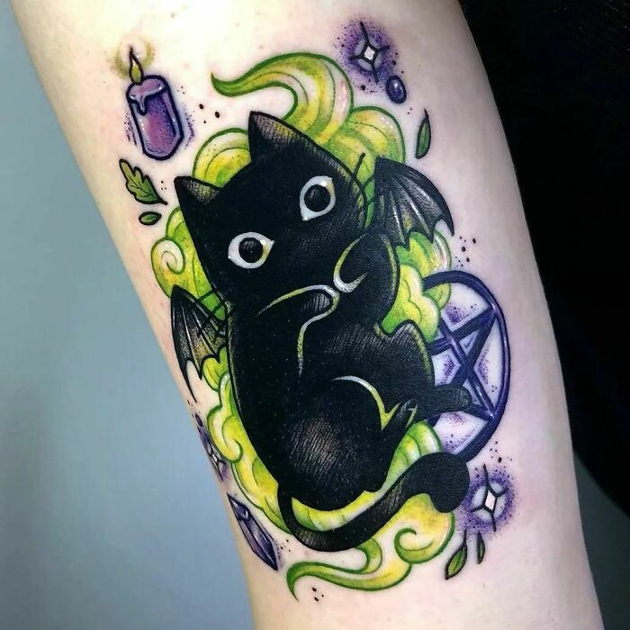 Cartoon tattoo of a cute black cat with wings, surrounded by colorful smoke and mystical symbols.