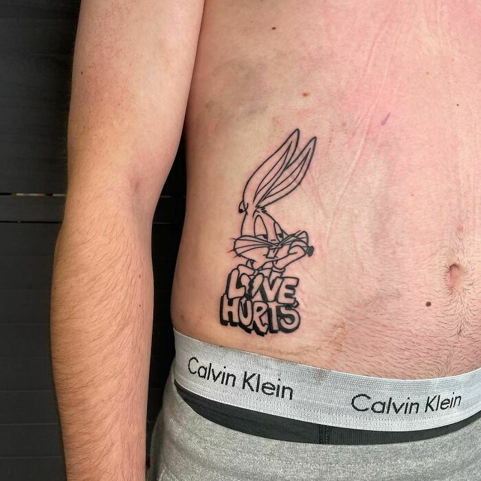 Cartoon tattoo of a classic animated character with "Love Hurts" text on a person's side torso.