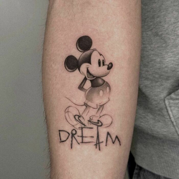 Cartoon tattoo of Mickey Mouse standing on "Dream" inscription, evoking nostalgia.