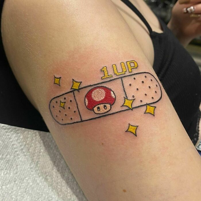 Cartoon tattoo featuring a 1UP mushroom on a bandage design, evoking childhood memories.