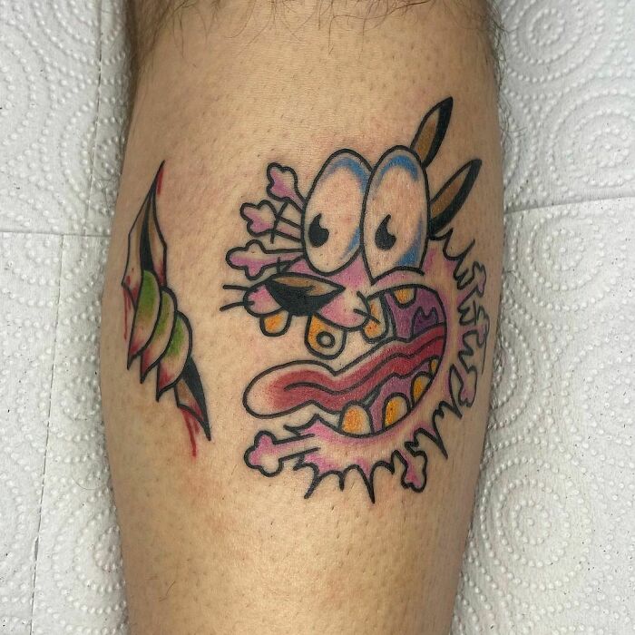 Cartoon tattoo of a quirky, wide-eyed character on a leg, inspired by animated shows.