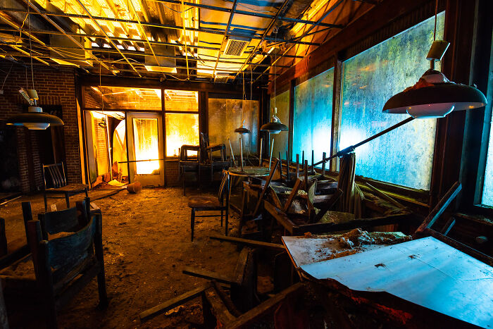 Interior of an abandoned place at night illuminated with bright artificial light showing old furniture and debris.