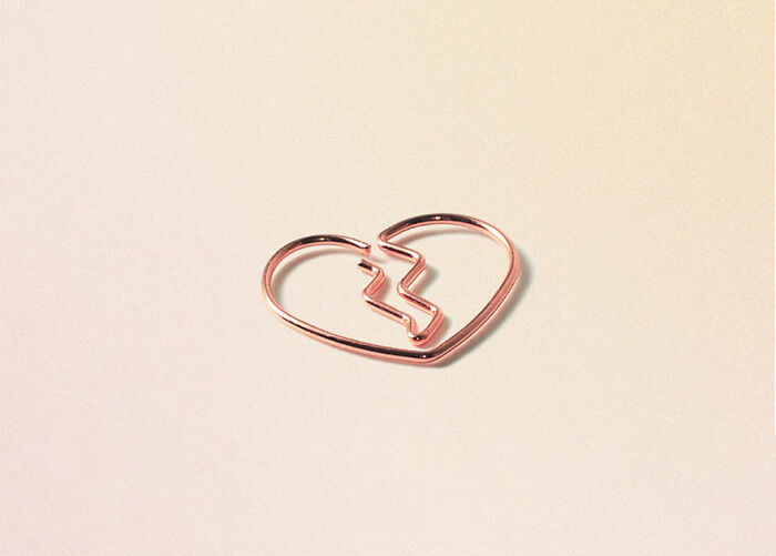 Unusual and conceptual product design of a rose gold broken heart-shaped paperclip on a light background.
