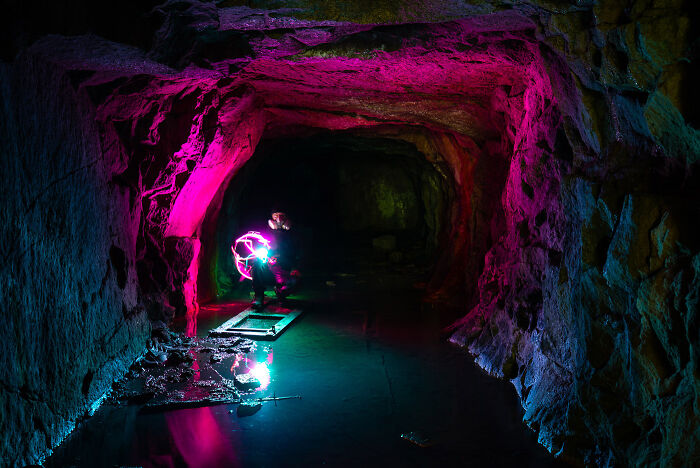 Person using bright light painting techniques inside an abandoned place at night with colorful illuminated cave walls.