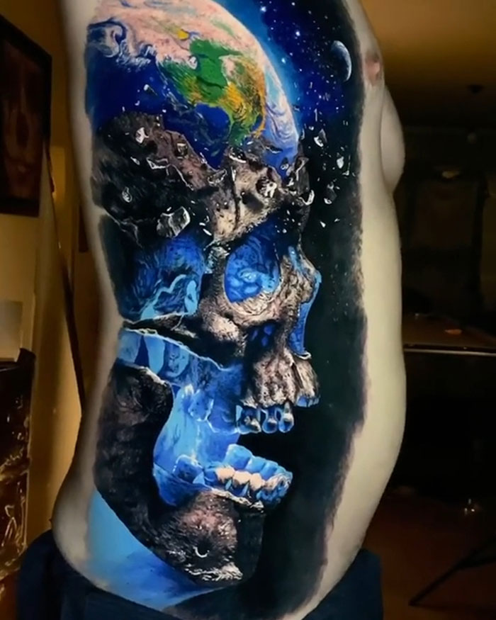 Colorful tattoo design of a skull merging with a planet on a person's side.