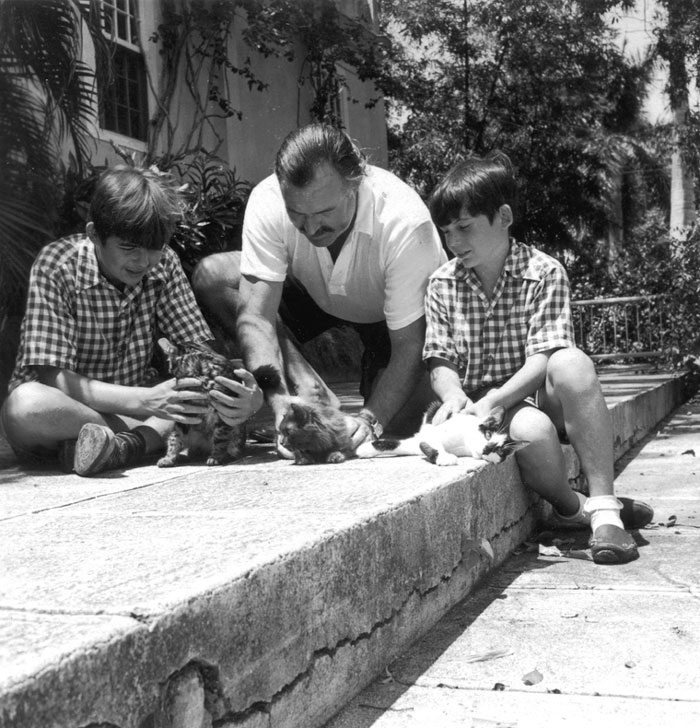 Ernest Hemingway and two young boys with polydactyl cats outisde