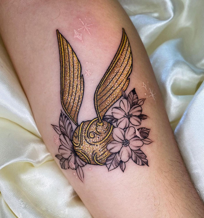 Golden snitch glitter tattoo with floral design on skin.