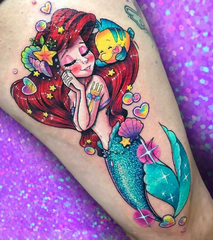 Mermaid glitter tattoo with colorful seashells and starfish adornments on a person's leg.