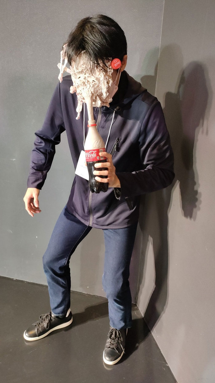 Person in mundane Halloween costume with soda explosion on face, holding a Coke bottle.
