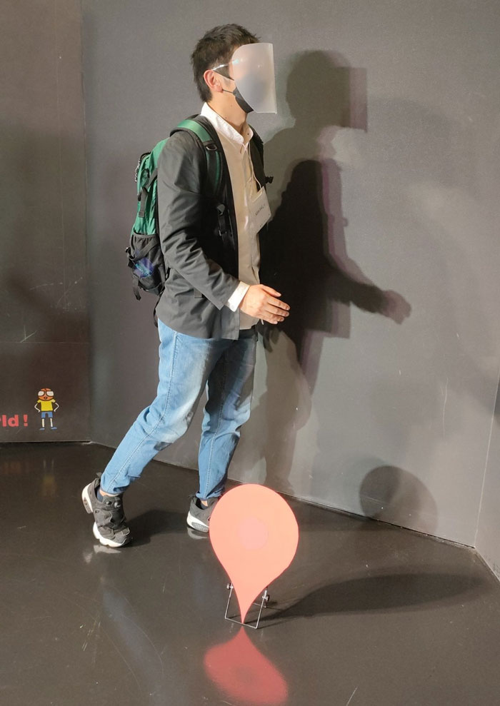 Person in mundane Halloween costume, dressed as a location pin with a red marker on the floor.