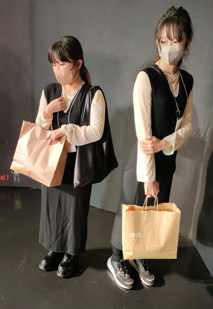 Two people in black and beige outfits with face masks, holding brown bags, showcasing mundane Halloween costumes.