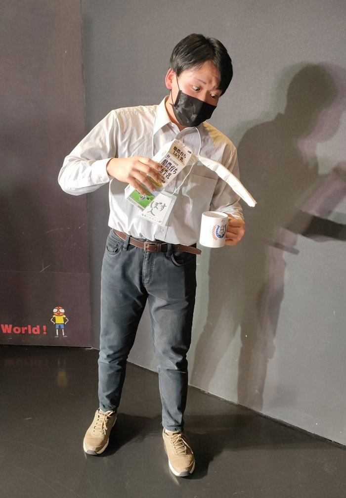 Person in "Mundane Halloween" costume spilling drink, wearing a mask and casual outfit, embodying a comically dull moment.