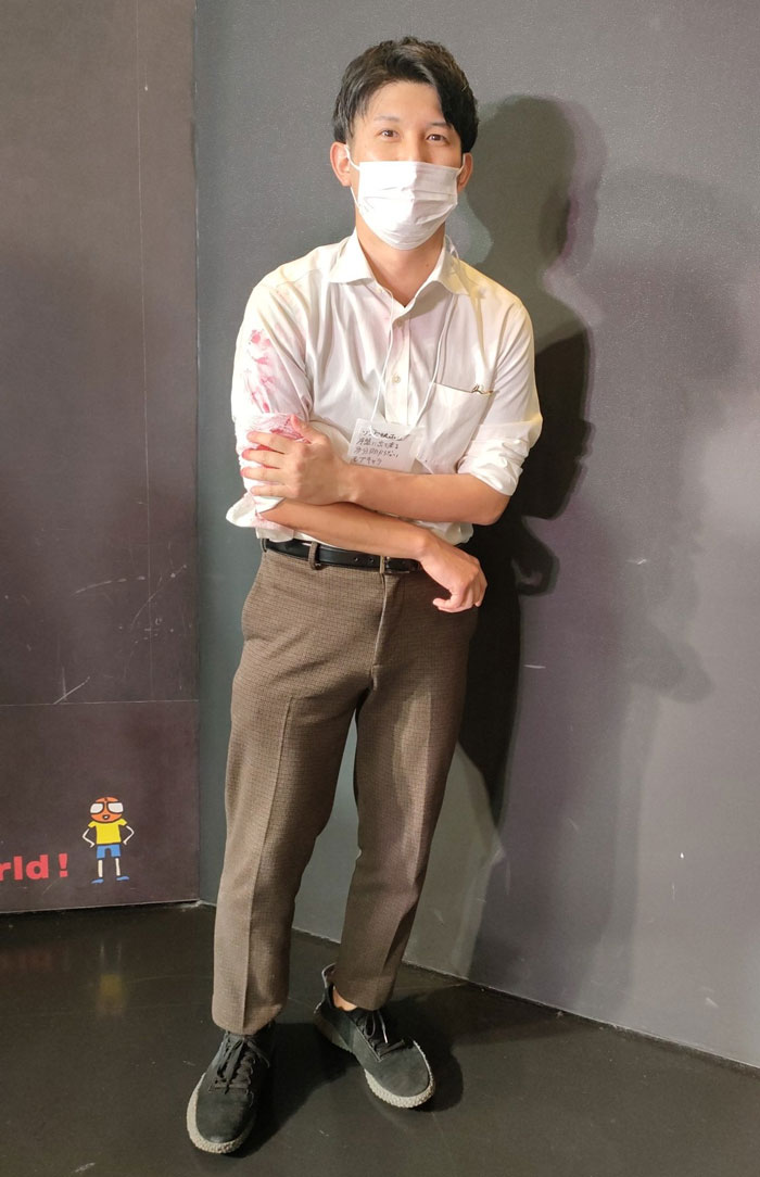 Man in mundane Halloween costume, wearing a white shirt, mask, and brown pants, with a slight arm stain.