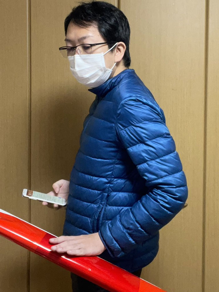 Person in a mundane Halloween costume, wearing a mask and blue jacket, looking at a phone while standing by a handrail.