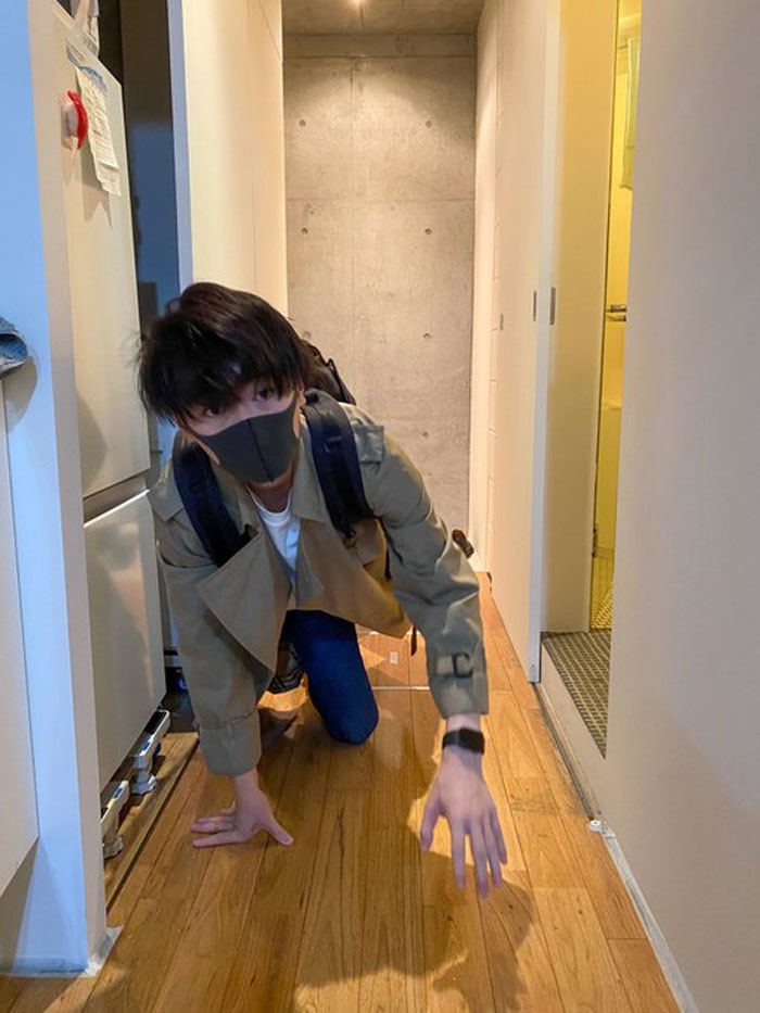 Person in a mundane Halloween costume crawling in a hallway, wearing a mask and trench coat.