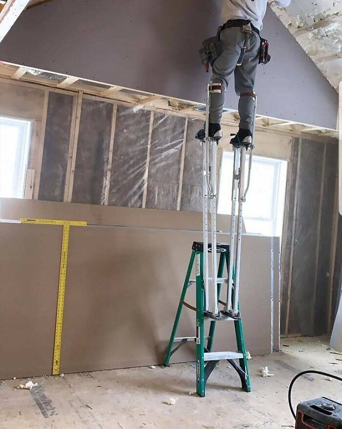 Person on stilts working on ceiling, standing on ladder, ignoring OSHA safety regulations.