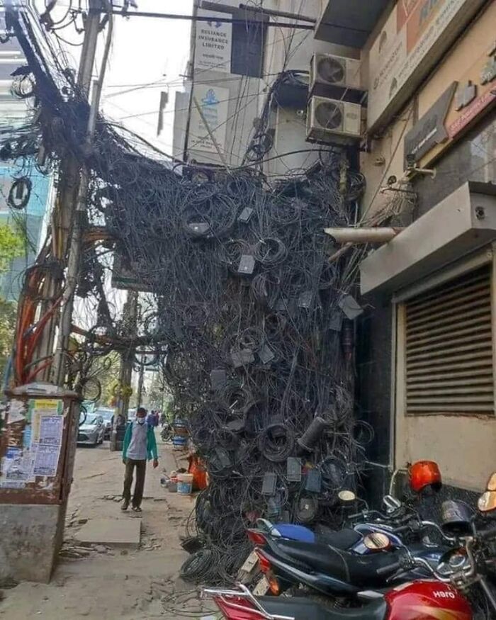 Unorganized cables hanging from a building, showing disregard for safety regulations, in a busy urban street scene.