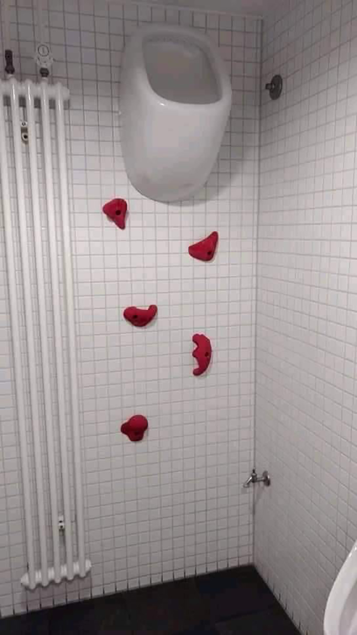 Urinal placed high on wall with climbing holds below, disregarding OSHA safety.