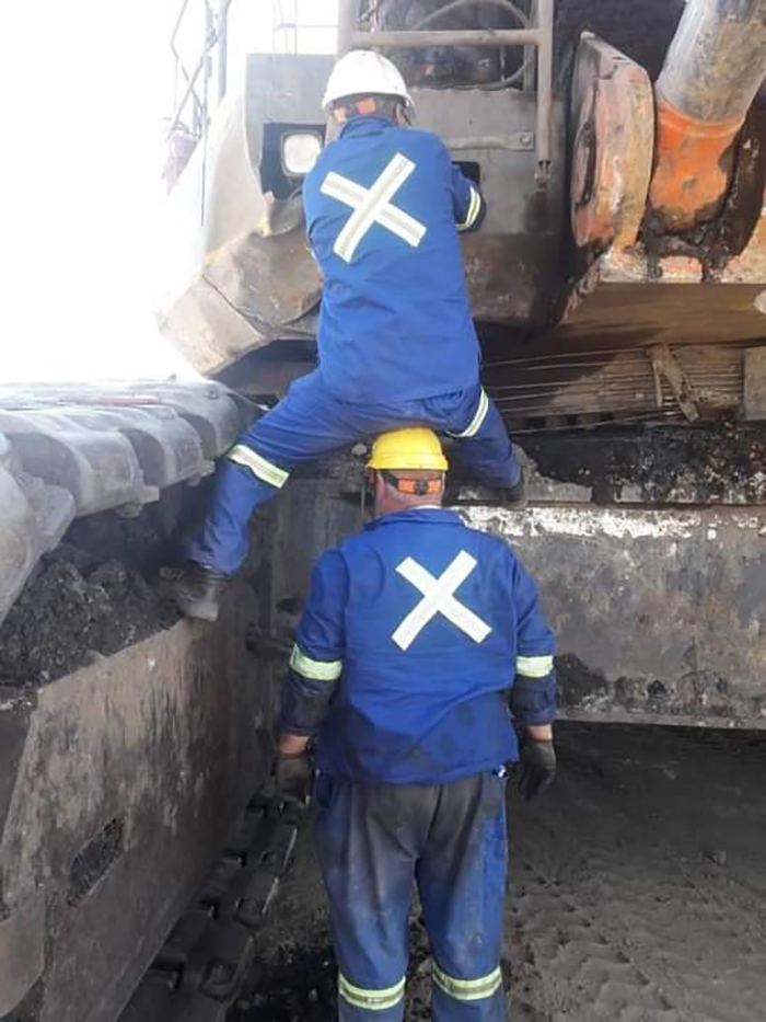 Two workers in blue safety gear using unconventional methods on heavy machinery, disregarding OSHA regulations.