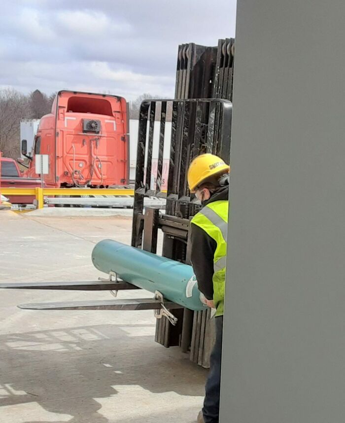 A worker in a hard hat using a forklift unsafely, ignoring OSHA safety regulations.