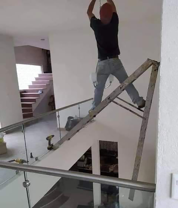 Unsafe work setup with a person balancing on a tilted ladder, ignoring OSHA safety regulations.