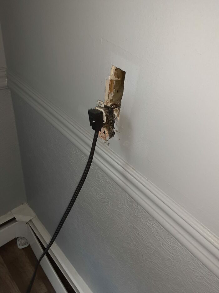 Unsafe electrical socket setup with exposed wires against a wall, ignoring OSHA safety regulations.